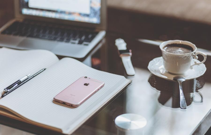 an open notebook on a desk in front of a laptop with a cup of coffee to the right