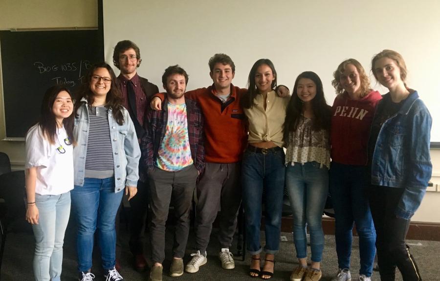 A picture of 9 graduating seniors seniors with their arms around each other, shown from the waist up. 